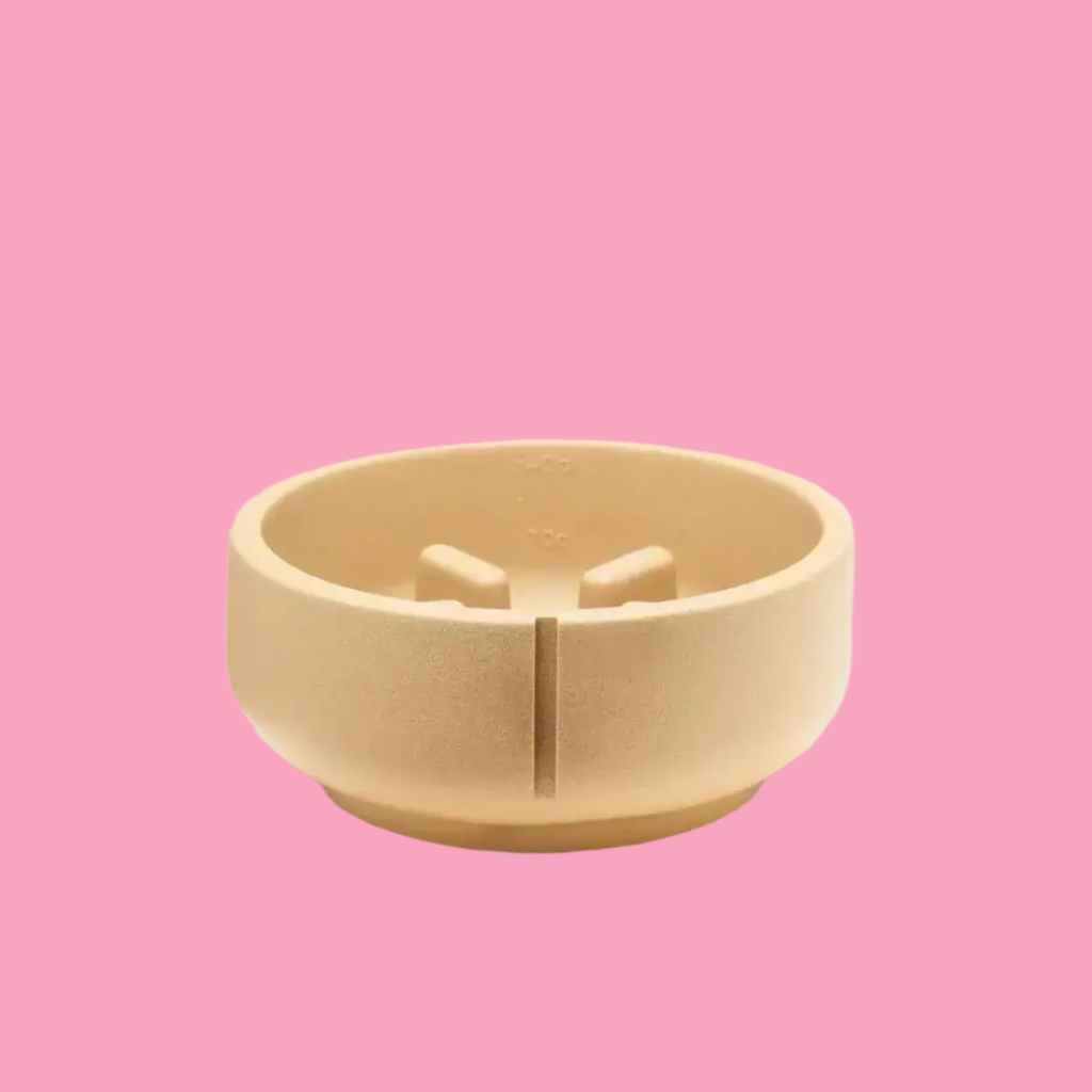 A beige, round, slow feeder dog bowl made of a heavy-duty material, placed on a white surface with a plain background.